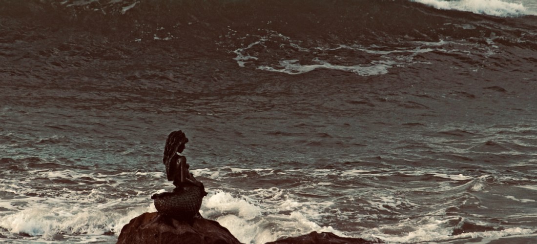 A statue of a mermaid sitting alone in the ocean.